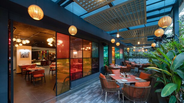 An indoor dining area with wicker furniture, glass partitions, and hanging lanterns. - Ira by Orchid Hyderabad Hitech City Mindspace IT Park (Hyderabad)