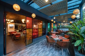Un espace de restauration intérieur aménagé avec des meubles en osier, des cloisons en verre et des lanternes suspendues.