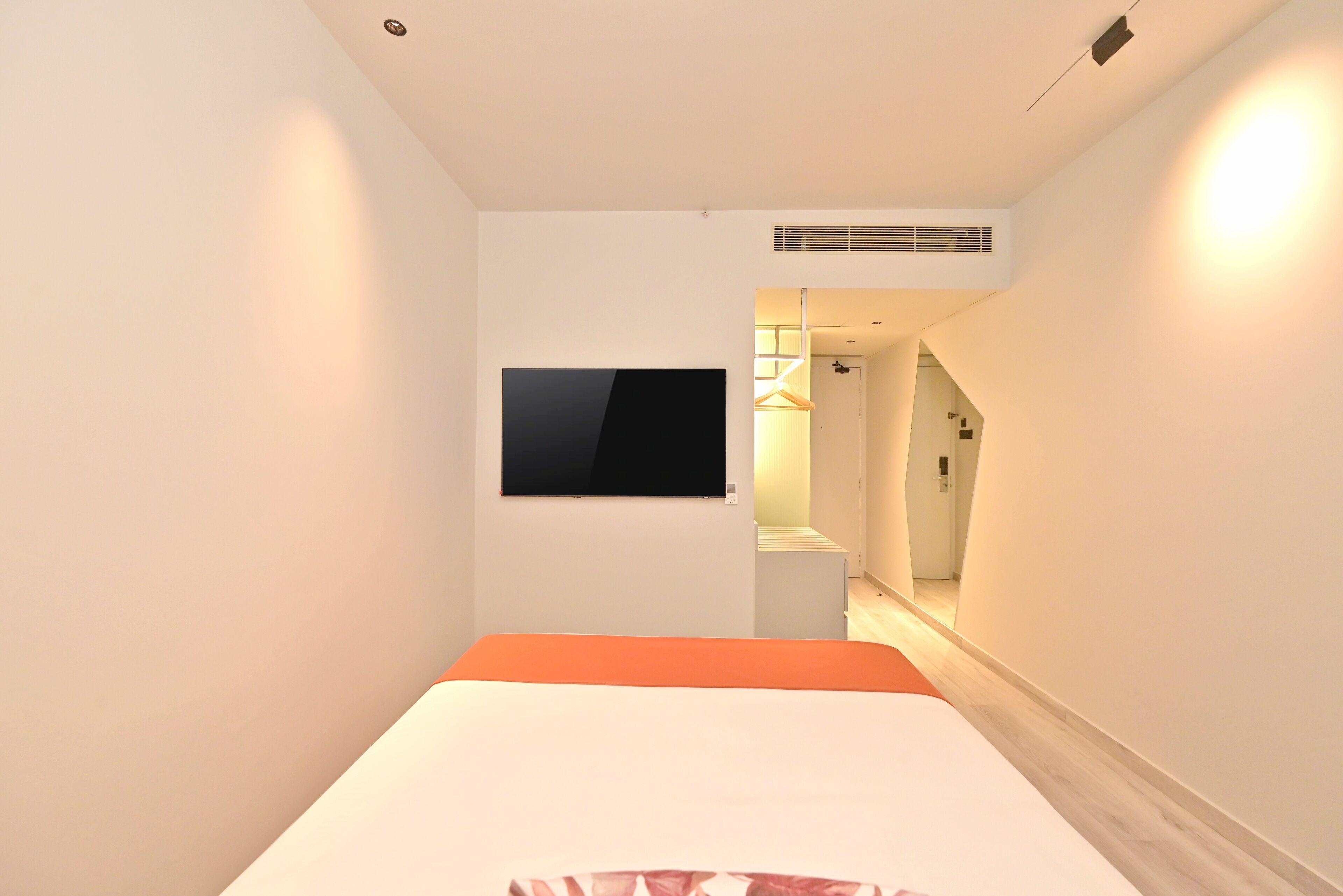 A hotel room with a bed, a TV mounted on the wall, and a hallway leading to a bathroom.