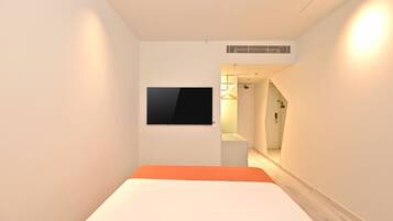 A hotel room with a bed, a TV mounted on the wall, and a hallway leading to a bathroom.