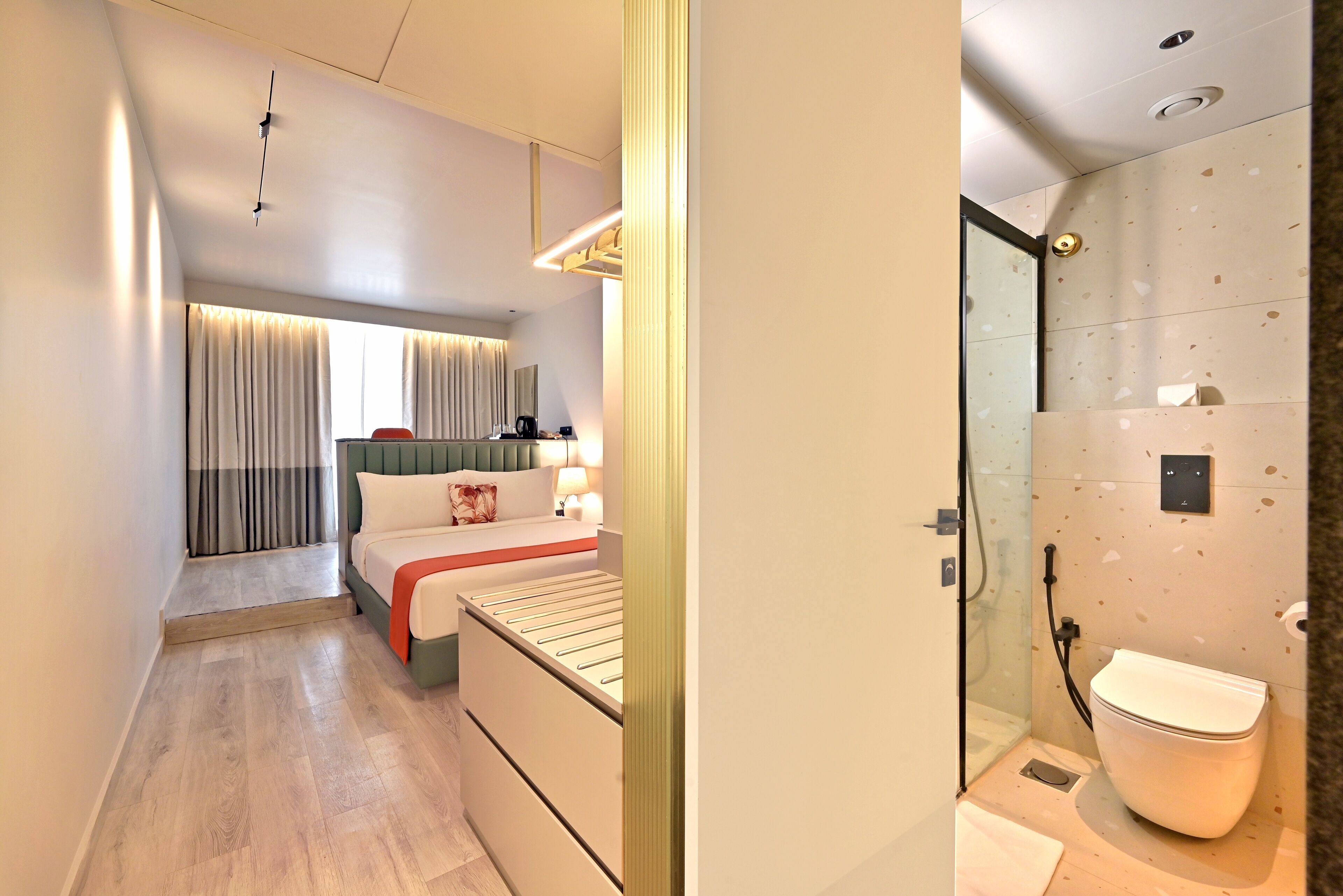 A modern hotel room with a bed, bedside table, and a shower area.