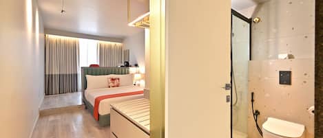 A modern hotel room with a bed, bedside table, and a shower area.