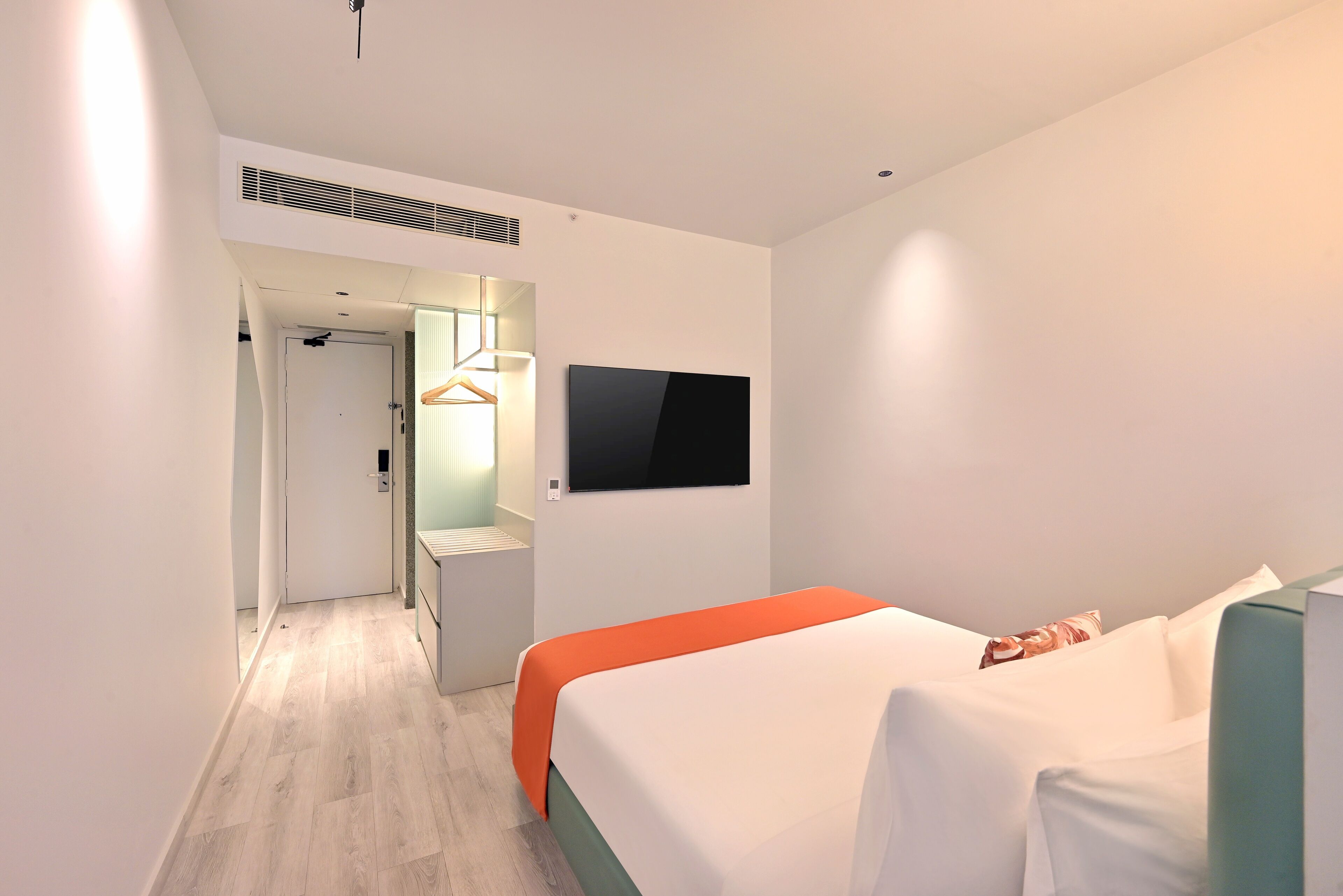 Een moderne hotelkamer met een bed, een aan de muur bevestigde televisie en een gang naar een badkamer.