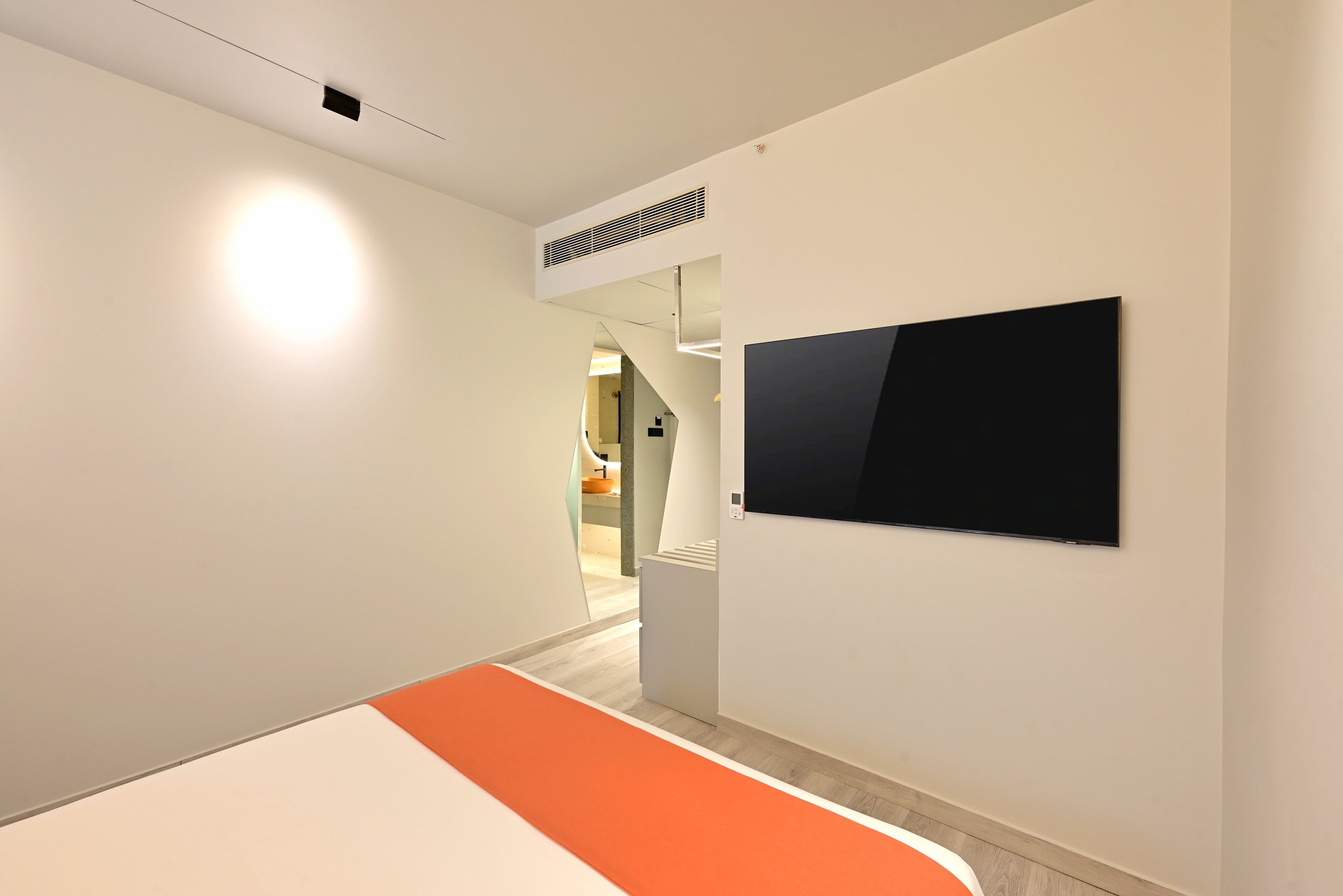 A modern hotel corridor with a flat-screen TV mounted on the wall, a bright light fixture on the ceiling, and a staircase leading to another area.