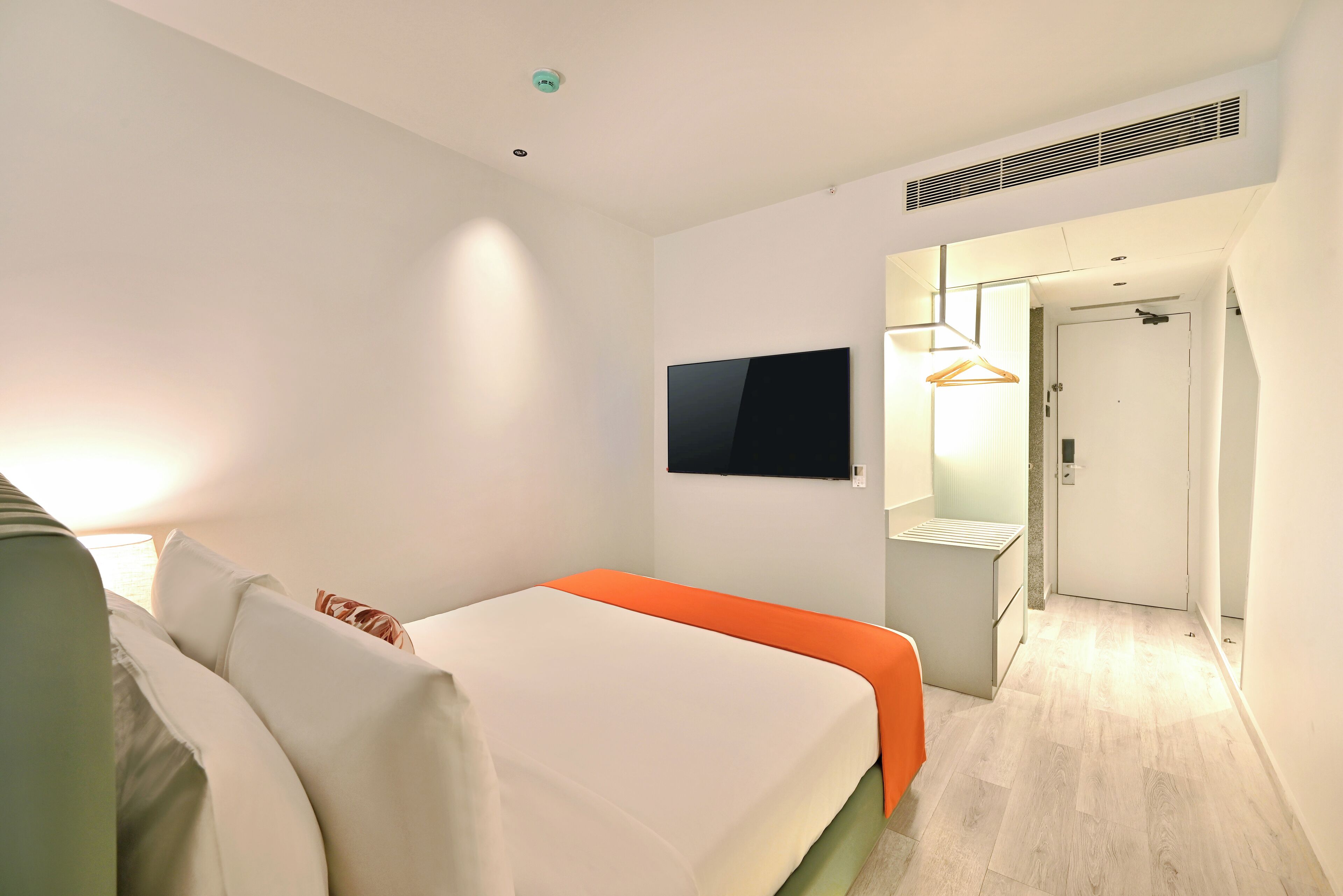 Ein modernes Hotelzimmer mit Bett, Flachbildfernseher, Nachttisch und begehbarem Kleiderschrank.
