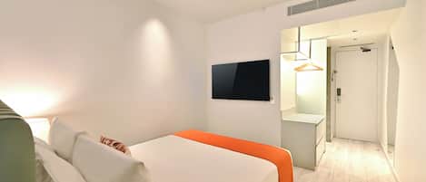 A modern hotel room with a bed, a flat-screen TV, a bedside table, and a walk-in closet.