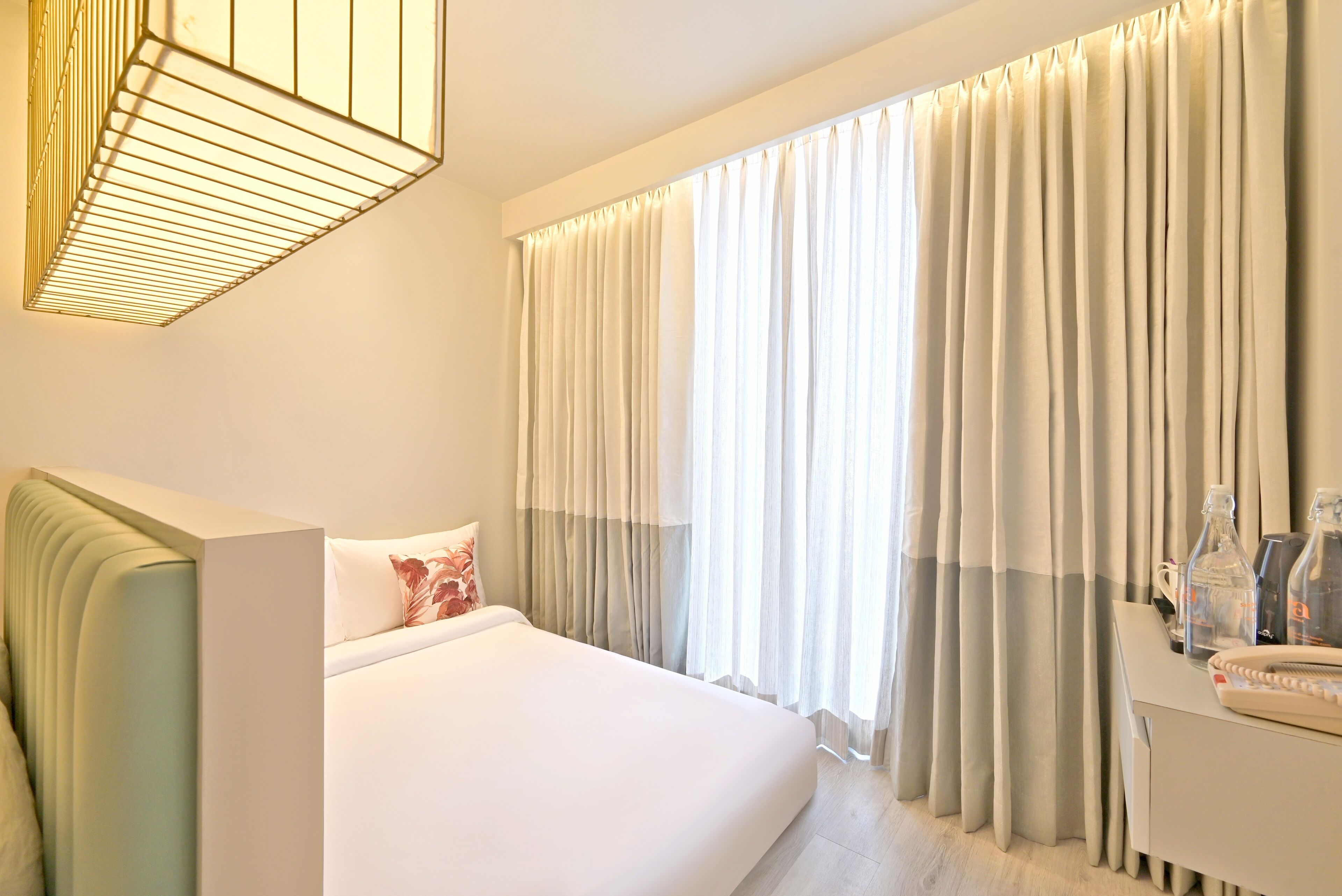 Une chambre d’hôtel avec un lit, une table de chevet avec une lampe et une fenêtre avec des rideaux.