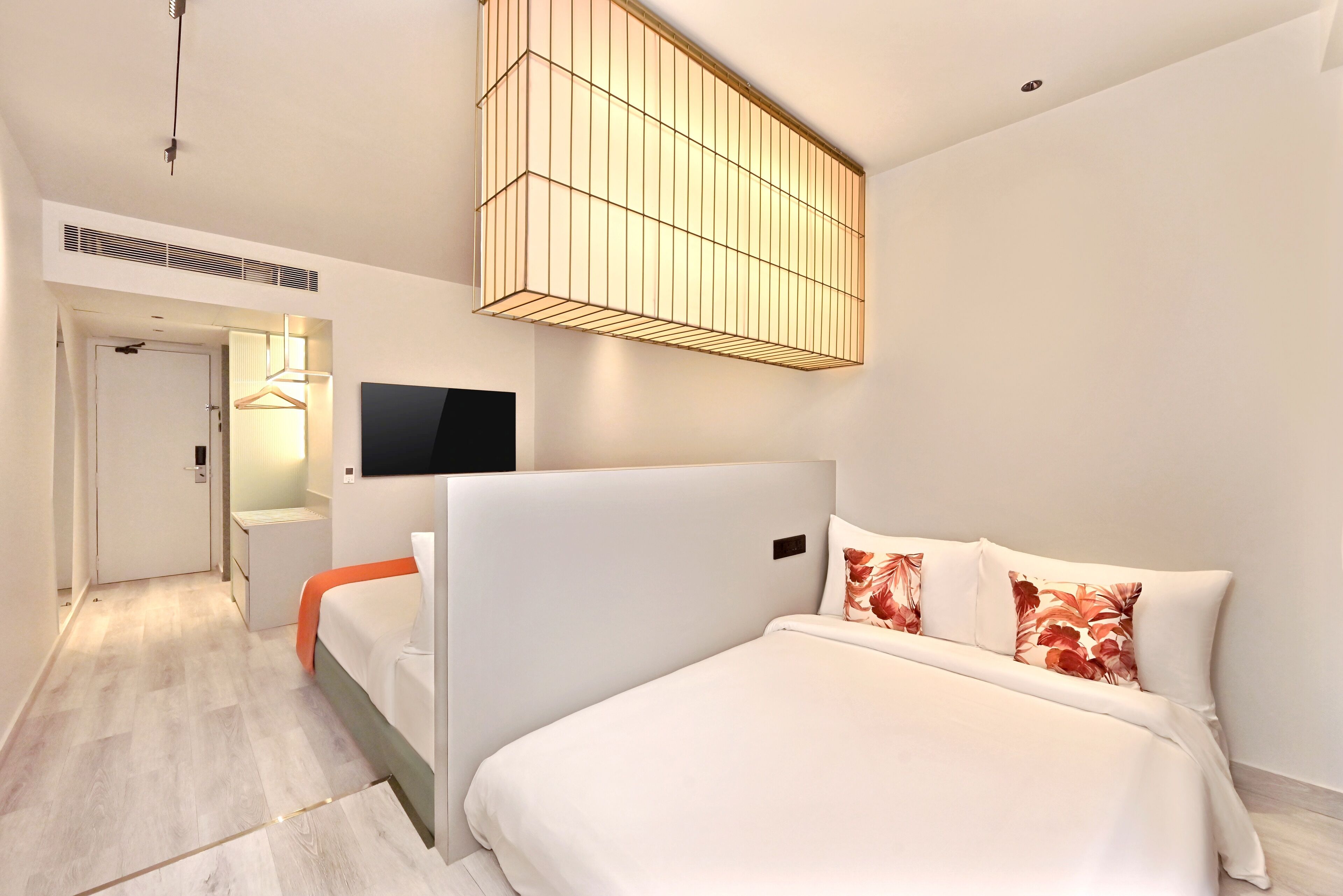 A modern hotel room with a large bed, a flat-screen TV, a ceiling light fixture, and a walk-in closet.