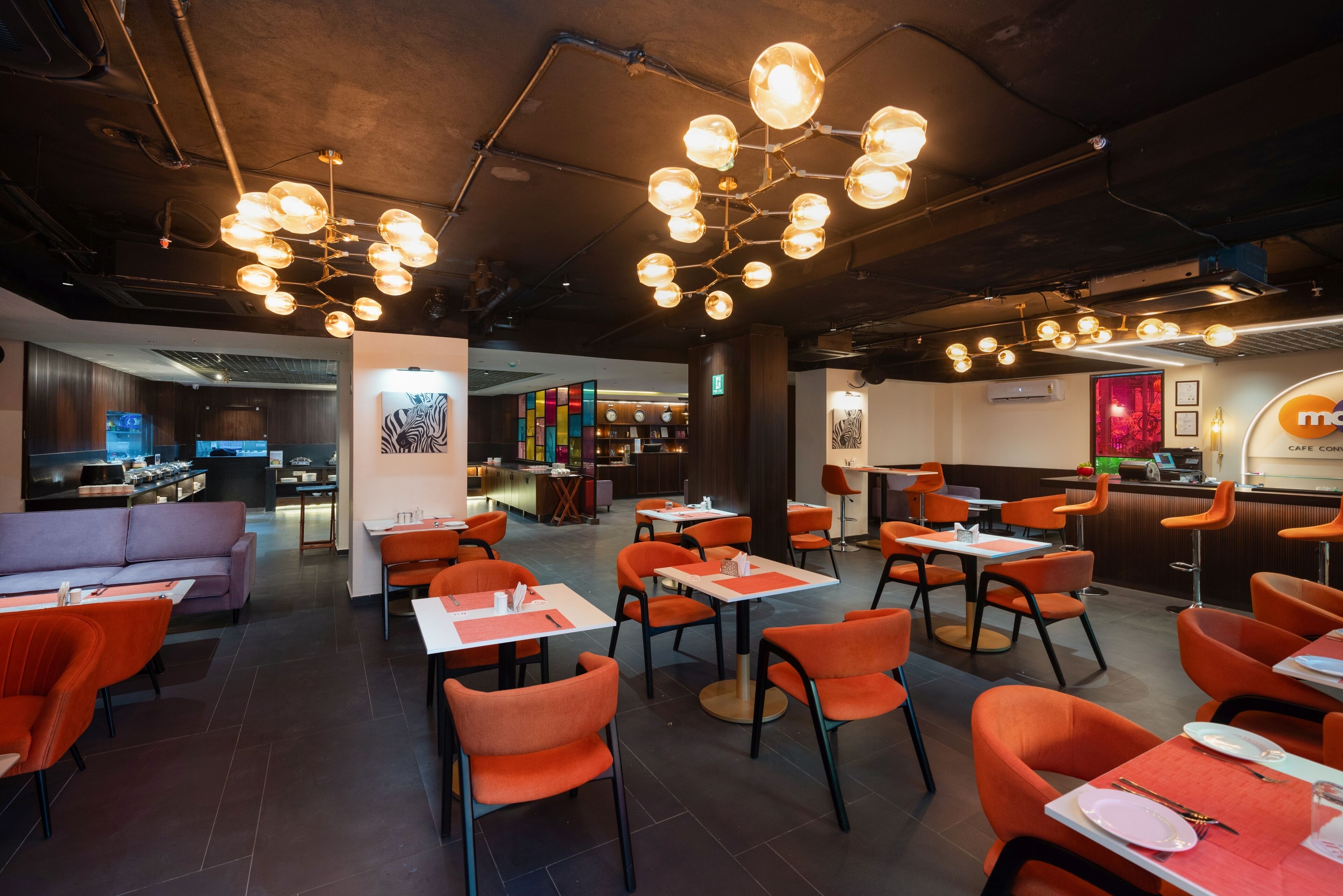 Un restaurant moderne avec des chaises et des tables orange, un coin bar et un tableau affichant le menu.