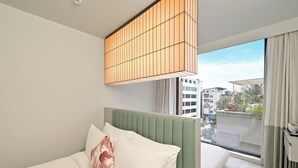 A modern hotel room with a large bed, a green headboard, a ceiling light fixture, and a view of the city through a large window. - Ira by Orchid Hyderabad Hitech City Mindspace IT Park (Hyderabad)