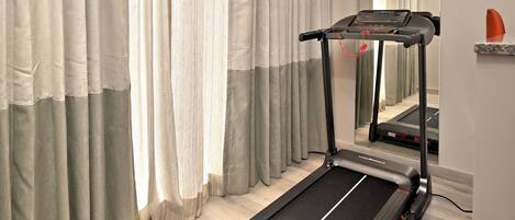 Une pièce équipée d’un tapis de course, d’un miroir et de rideaux.