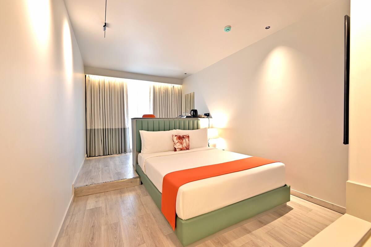 Una habitación de hotel moderna con cama, mesita de noche, lámpara y ventana con cortinas.