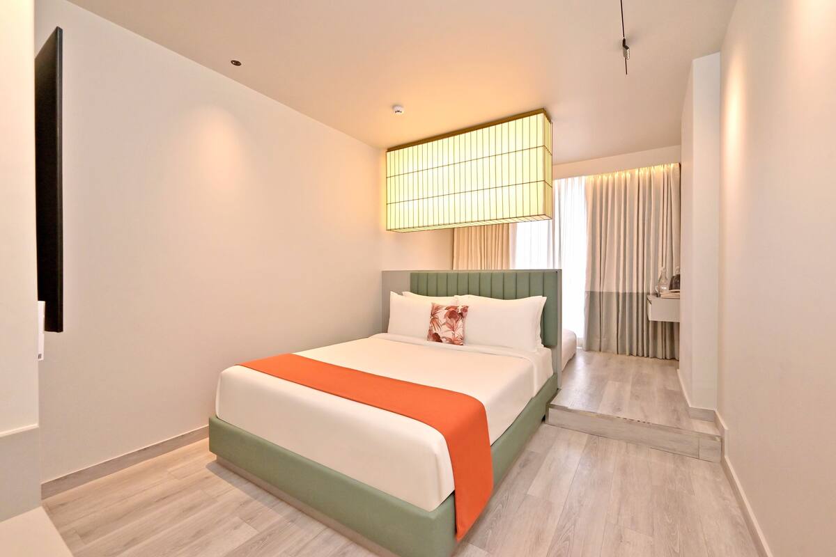 Una habitación de hotel moderna con una cama grande, una mesita de noche, un espejo y una ventana con cortinas.