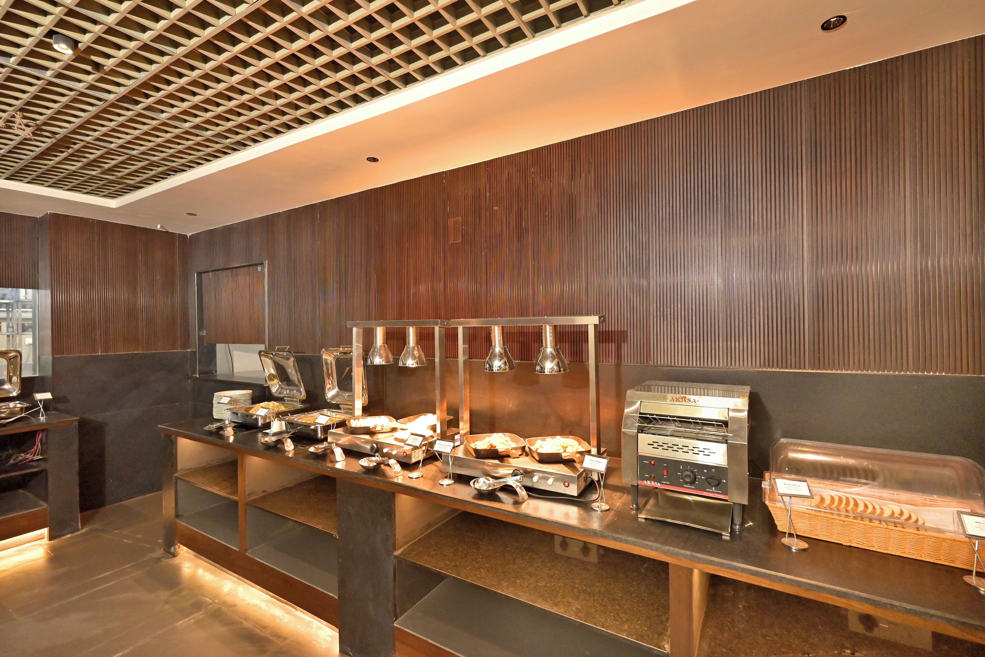 Een buffetopstelling met diverse gerechten, een koffiemachine voor zelfbediening en een zithoek met een comfortabele bank.