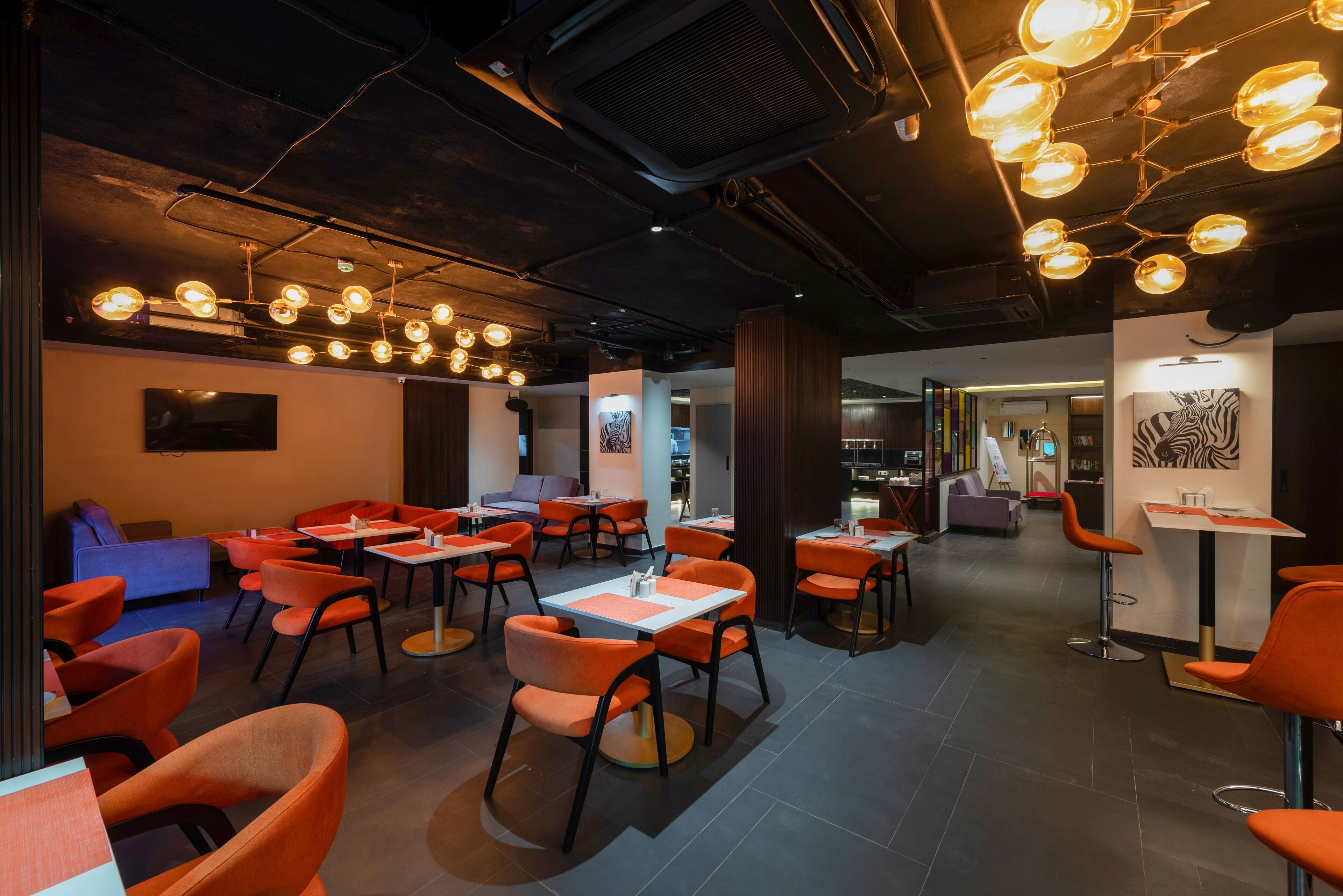 Ein modernes Interieur mit orangefarbenen Sesseln und Tischen, einer Decke mit hängenden Lampen und Kunstwerken an den Wänden.