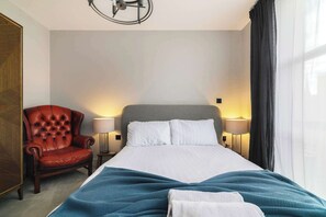 Habitación de hotel con cama, sillón de cuero rojo, dos lámparas de noche y un amplio ventanal con cortinas.