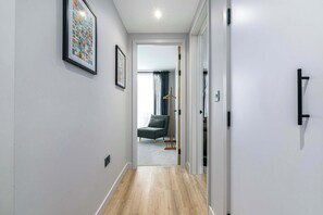 A hallway with a wooden floor, a grey chair, and a coat rack.