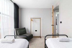 A hotel room with two beds, a chair, a wooden wardrobe, and a door leading to another room.