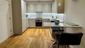 Une cuisine moderne avec un plancher en bois, des armoires blanches, un tabouret de bar noir et un ordinateur portable posé sur le comptoir.