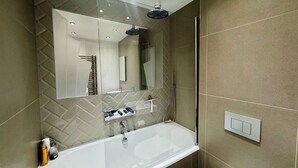 Une salle de bain moderne avec une baignoire entourée de parois en verre, un grand miroir et une pomme de douche.