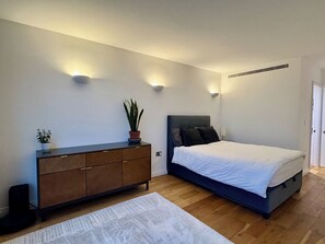 A bedroom with a bed, a dresser, a potted plant, and wall-mounted lighting.