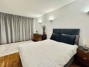 A modern bedroom with a large bed, a nightstand, a dresser, and a potted plant. - Designer 1 Bed Flat in Iconic Building (Perivale)