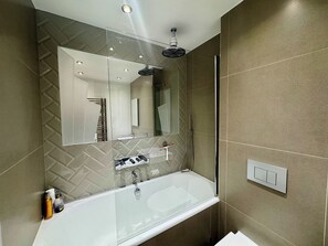 A modern bathroom with a glass-enclosed bathtub, a large mirror, and a showerhead.