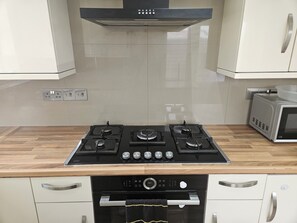Cocina con estufa a gas, horno, microondas y gabinetes blancos.
