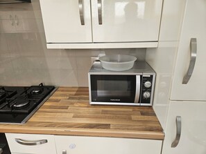 A kitchen with a microwave, a gas stove, and white cabinets. - Bright 3BD House Near East Croydon Station (Greater London)