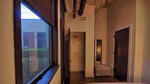 A bedroom with a large window, a door leading to a bathroom, and a small bedside table. - Chic Ultramodern Minimalist Loft Suite + Patio (Saint Louis)