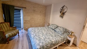 A bedroom with a bed, a chair, a bedside table, a wall decoration, and a window with curtains. - Le Figuier:8-person gite, heated pool and leisure facilities 25 minutes from Futuroscope. (Mazeuil)