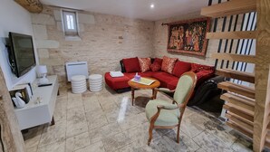 A cozy living room with a red sofa, a wooden chair, a television, and a stone wall. - Le Figuier:8-person gite, heated pool and leisure facilities 25 minutes from Futuroscope. (Mazeuil)