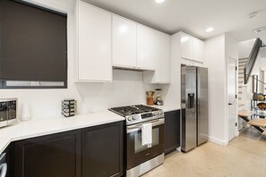 Une cuisine moderne avec des meubles blancs, une cuisinière en acier inoxydable et un réfrigérateur.