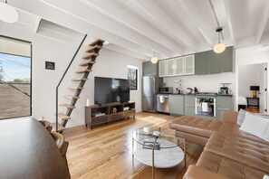 Una sala moderna con una escalera, un televisor de pantalla plana, una mesa de centro de vidrio y un sofá de cuero.