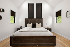 A modern bedroom with a large bed, two bedside tables, and a window with a view of trees. - Austin Luxury 5BR Modern House | by Barclé (Austin)