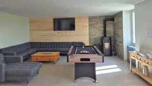 A modern living room with a pool table, a sofa, and a television mounted on the wall. - Gîte de La Berthuinière (Saint-Martin-en-Vercors)