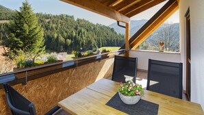 Una mesa de madera con sillas, un florero y vistas a una cadena montañosa boscosa.