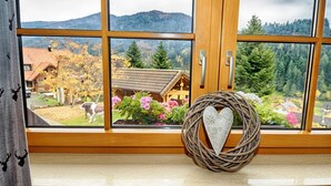 Una ventana con vistas a una montaña, una cabaña de madera y una cesta decorativa con forma de corazón.