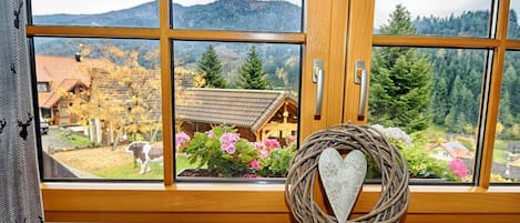 A window with a view of a mountain, a wooden cabin, and a decorative heart-shaped basket.