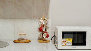 Una cocina con microondas, especiero y un frasco de vidrio sobre un posavasos de madera.