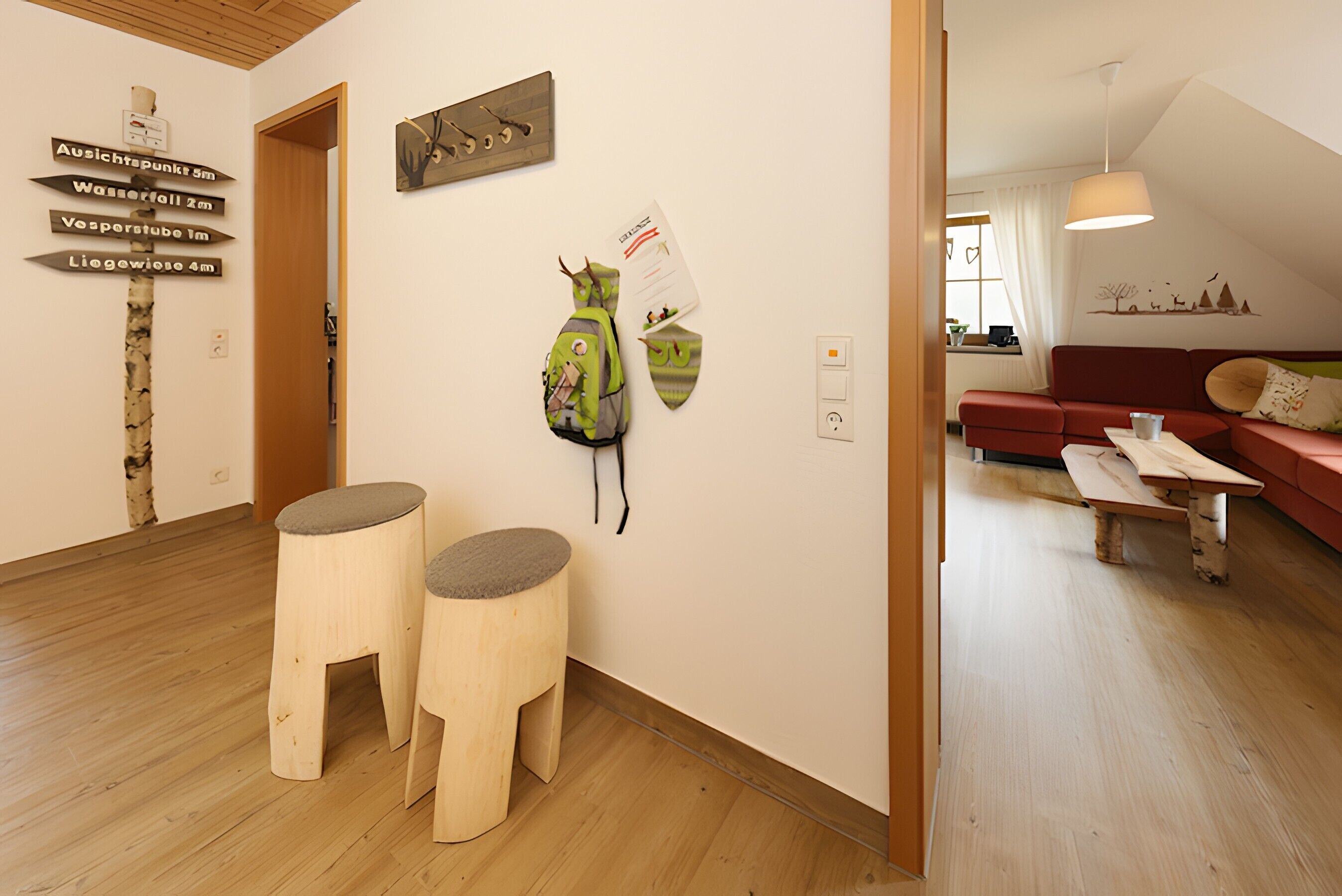 A room with a wooden floor, a red sofa, a wooden bench, and a wall-mounted backpack.