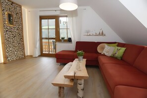 Una sala moderna con un sofá rojo, una mesa de madera y vistas al exterior a través de un ventanal grande.