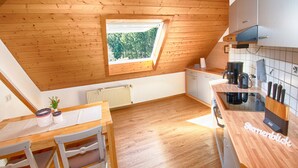 Una cocina con suelo de madera, una mesa de comedor con sillas, una ventana con vistas a árboles y un salpicadero de azulejos.