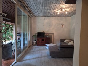 Un salón con chimenea, televisor, sofá y puerta de cristal que da a un espacio exterior.