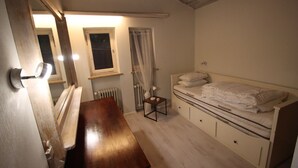 A bedroom with a wooden bed, a small bedside table, a chair, a window with curtains, and a radiator.