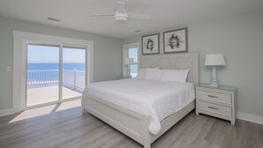 A bedroom with a large bed, a nightstand, a ceiling fan, and a view of the ocean through a sliding door. - 7 Bedroom, Ocean Front Paradise - 1 To Sea (Garden City)