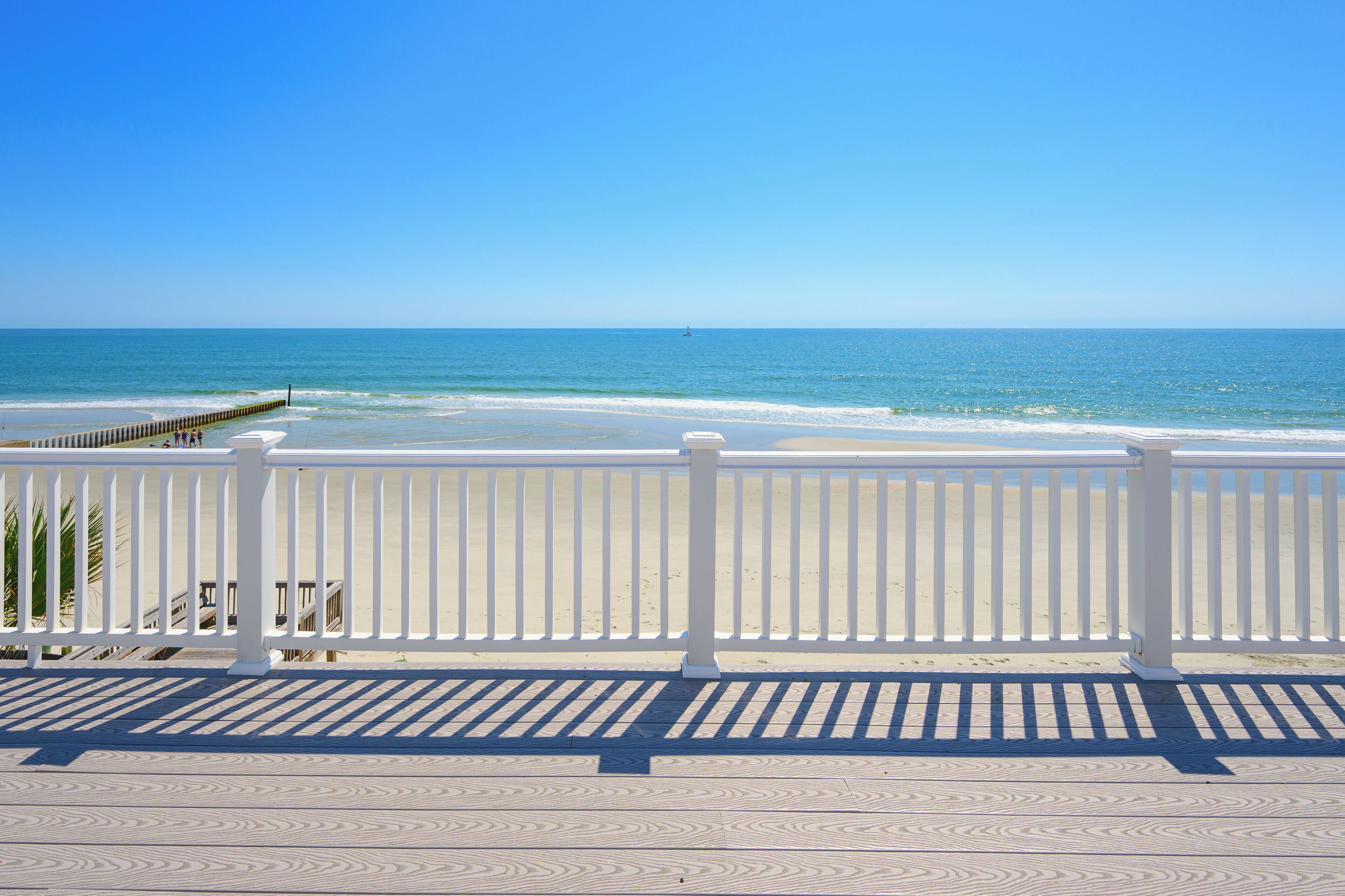 A beach view with a white fence and a wooden pier.