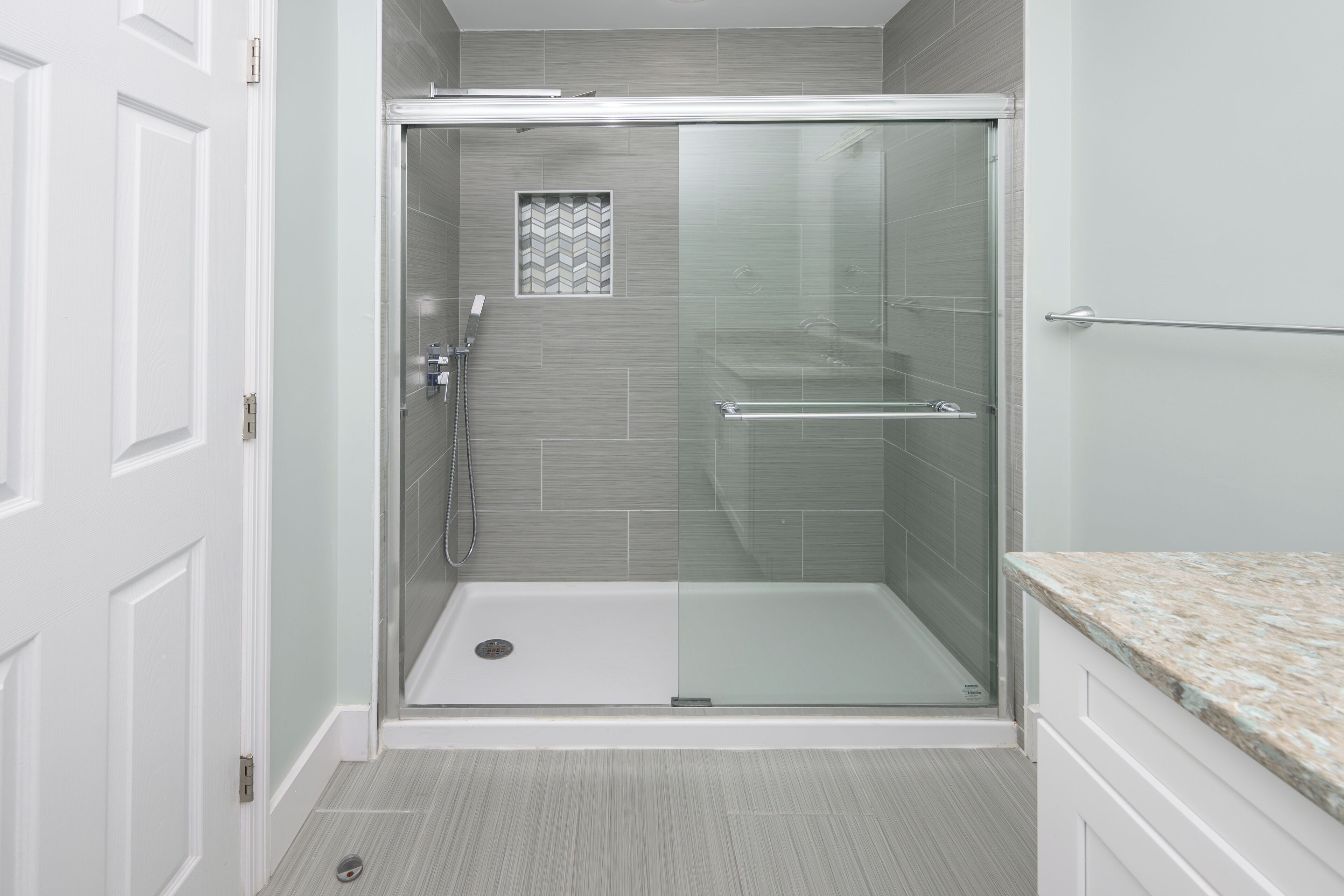 A walk-in shower with a glass door, a small vent on the wall, and a tiled floor.