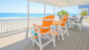 A covered outdoor seating area with wooden flooring, white railings, and orange chairs. - 7 Bedroom, Ocean Front Paradise - 1 To Sea (Garden City)