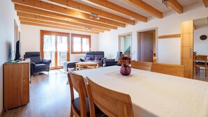 Amplia sala de estar con techo de madera, una mesa de comedor con sillas, un sofá y un televisor sobre un mueble.